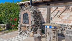 A stone-built outdoor oven with a brick wall and wooden logs nearby.