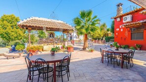 An outdoor patio area with round tables and chairs, a stone fountain, and a red building with a tiled roof. - El Secanillo Loja by Ruralidays (Granada)