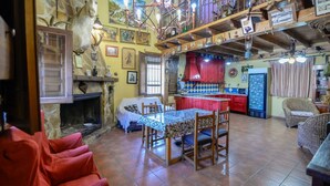 A rustic interior with a stone fireplace, a dining area with a patterned tablecloth, and a kitchen with red cabinets.
