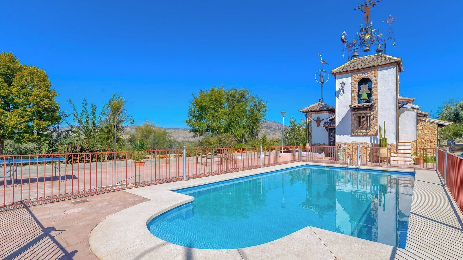 A swimming pool with a fenced area, a small bell tower, and a clear blue sky.