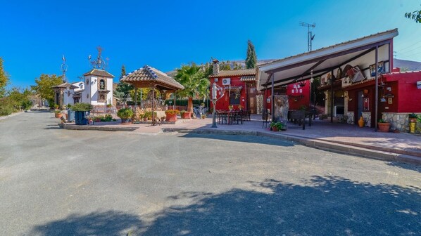 A street view with a small chapel, a red building with outdoor seating, and a clear blue sky.