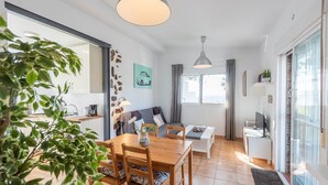 Moderni olohuone, jossa on ruokailutila, sohva, televisio ja avoimen oven kautta näkyvä keittiö.
