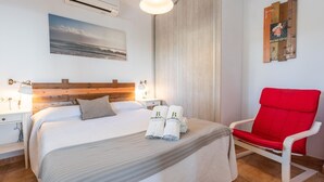 Hotellihuone, jossa on sänky, punainen tuoli, rantamaisemaa esittävä taulu ja puinen pääty.
