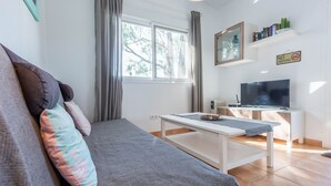 Moderni olohuone, jossa on sohva, sohvapöytä, televisio ja kirjahylly.