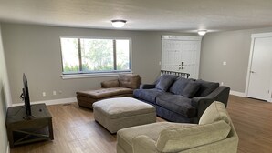 A living room with a sectional sofa, an ottoman, a TV on a stand, and a window with blinds. - Perfect for Long Stays. Recently remodeled townhouse next to Freeway & C of I.  (Caldwell)