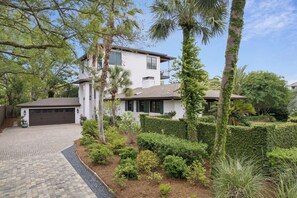 Ein modernes, zweigeschossiges Haus mit Garage, umgeben von gepflegter Bepflanzung mit Hecken und Palmen.