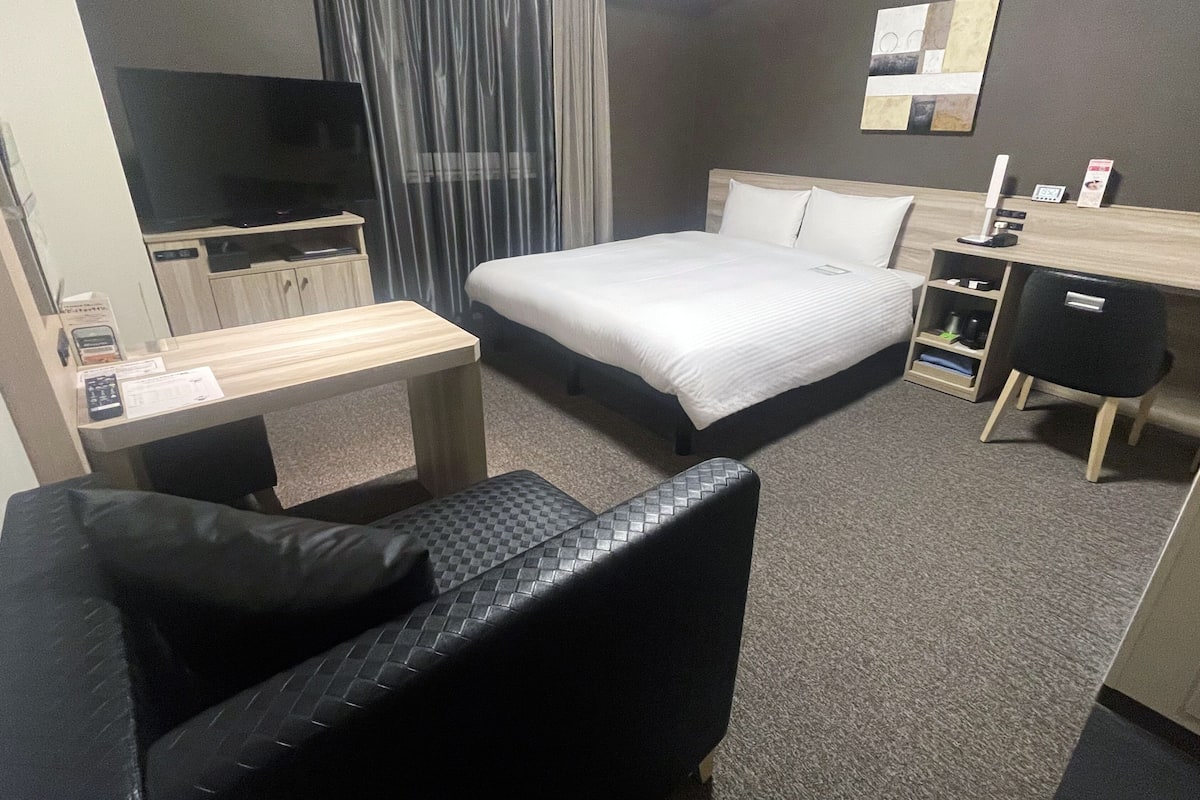 A hotel room with a bed, a desk, a chair, a television, and a window with curtains.