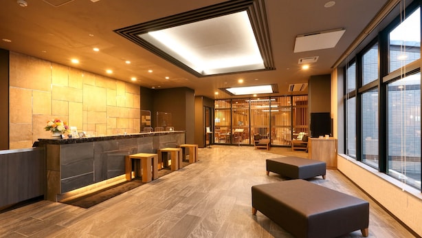 A modern hotel lobby with a reception desk, seating area, and large windows. - Route Inn Grantia Tokai Spa & Relaxation (Tokai)