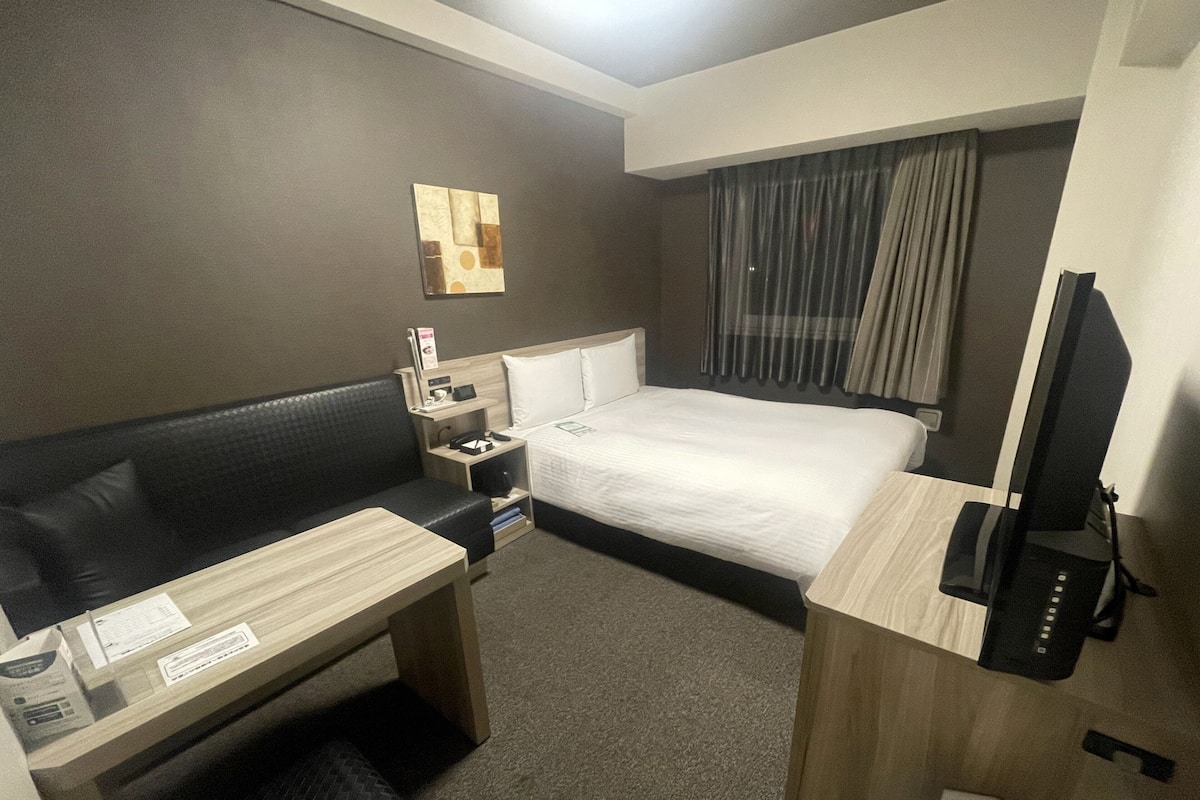 A hotel room with a bed, a desk, a chair, a TV, and a wall-mounted artwork.