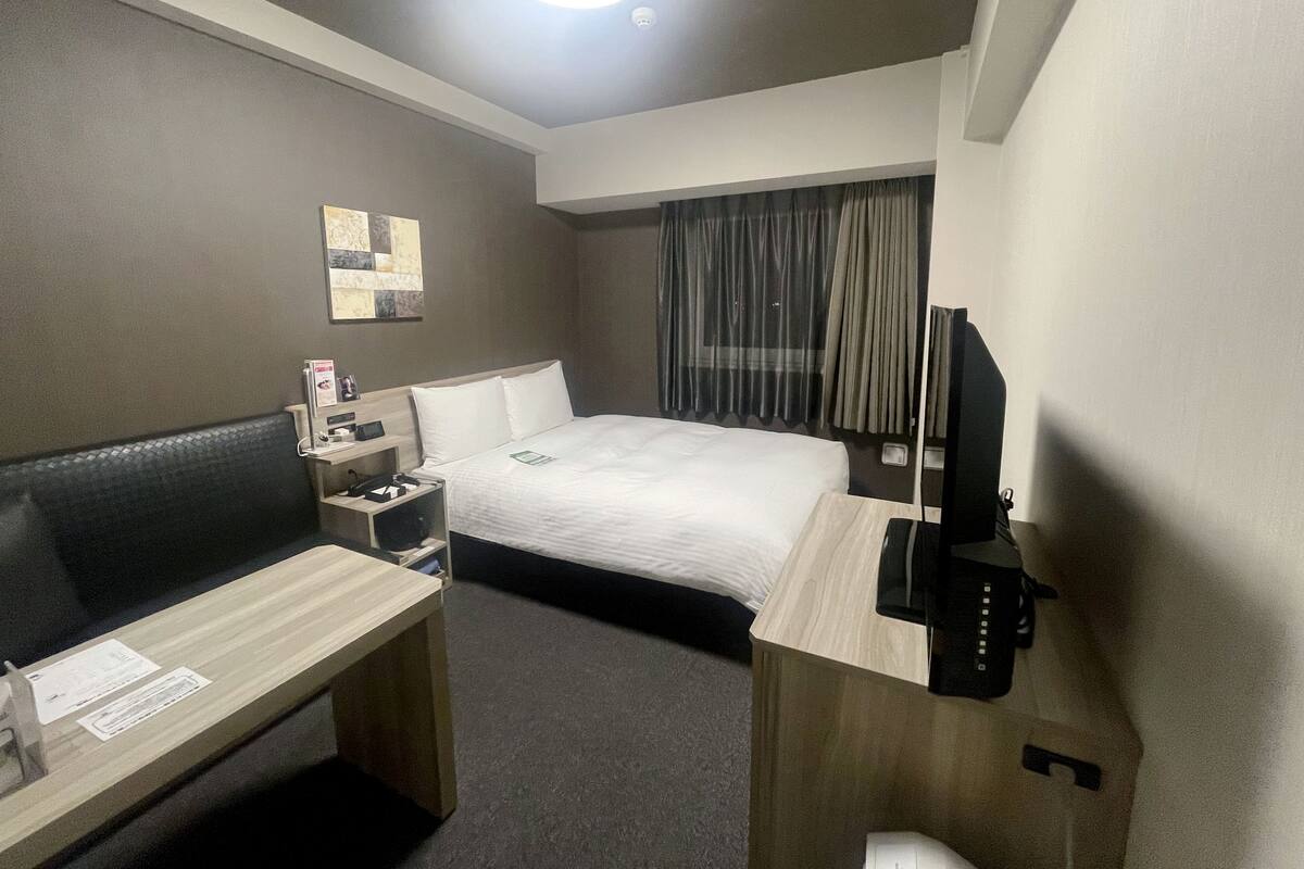 A hotel room with a bed, a desk, a television, and a window with curtains.