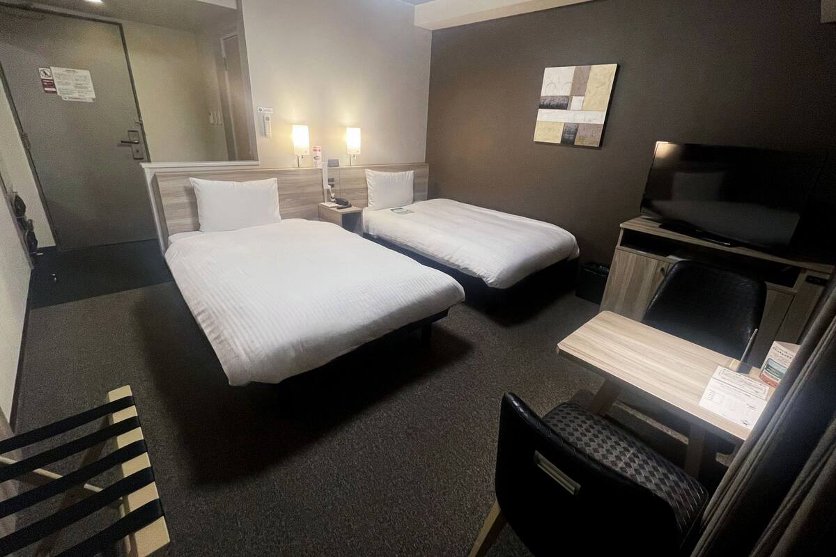 A hotel room with two single beds, a desk with a chair, a TV, and a small table.