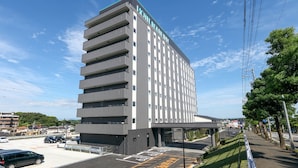 A multi-story hotel with a modern design, featuring a prominent entrance and a parking area. - Route Inn Grantia Tokai Spa & Relaxation (Tokai)