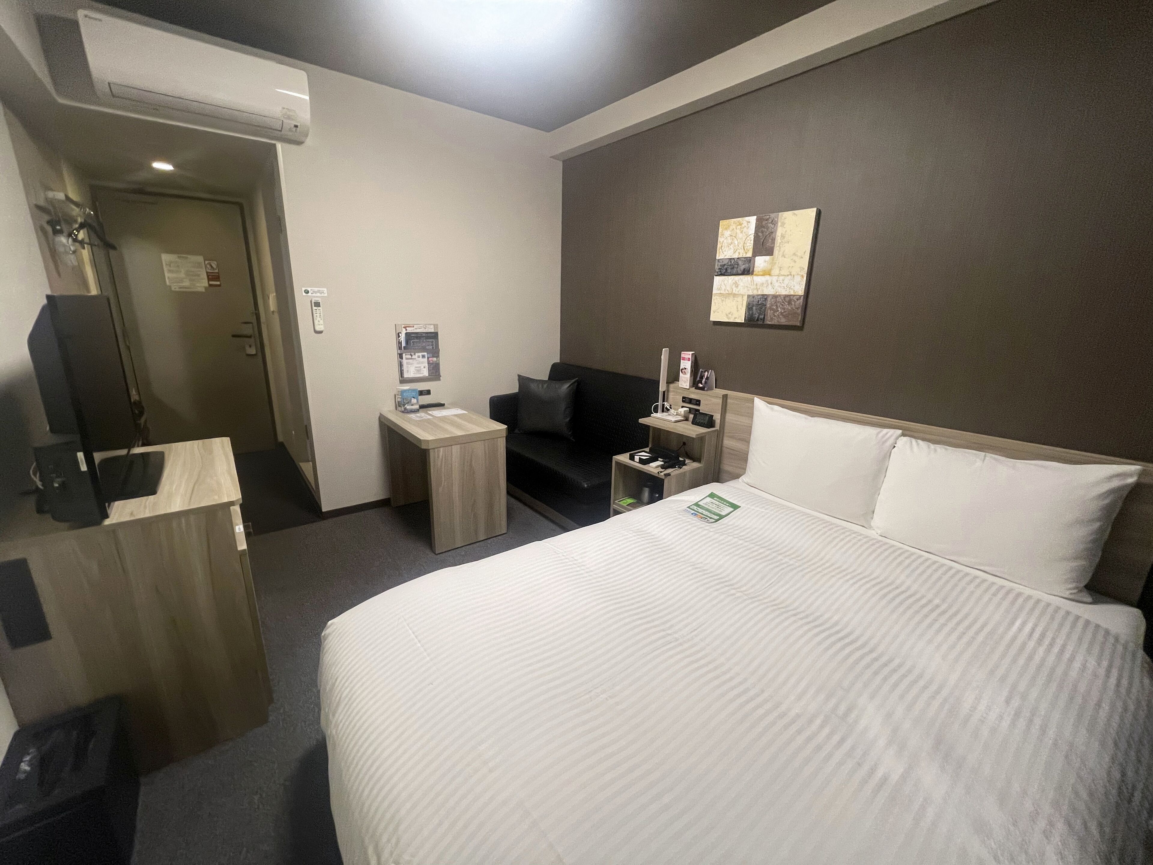 A hotel room with a large bed, a desk, a chair, a TV, and a small table.