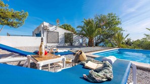 Un espace aménagé au bord de la piscine, avec des chaises longues, une bouteille de vin et un livre.