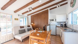 Ein gemütliches Zimmer mit Holzbalkendecke, einer Couch, einem Esstisch und einer Küchenzeile mit Kühlschrank und Mikrowelle.