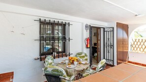 A dining area with a table set for two, chairs, a window with bars, and a door leading to another room.