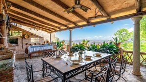 Eine Terrasse im Freien mit Esstisch und Stühlen, umgeben von Pflanzen in Töpfen.