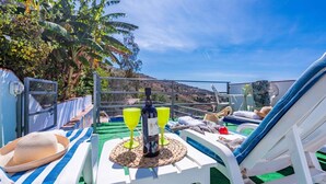 Un espace extérieur ensoleillé, aménagé avec des fauteuils confortables, une table avec une bouteille et des verres, et offrant une vue sur le paysage.