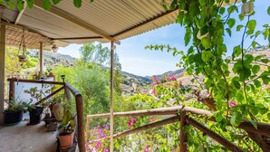 Un espace extérieur abrité, agrémenté de plantes en pot, d’une clôture en bois et offrant une vue sur un paysage vallonné.