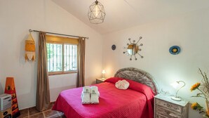 Une chambre à coucher avec un lit, une table de chevet, une lampe, un miroir et une fenêtre avec des rideaux.