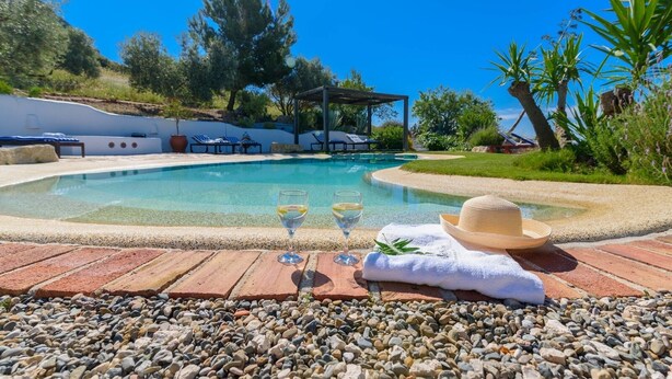 A poolside area with a lounge chair, a sun umbrella, and a hat on a towel.