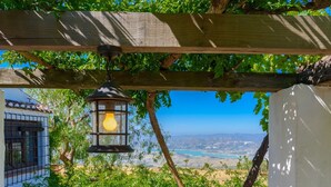 A wooden pergola with a hanging lantern, a view of a coastal landscape, and a building with barred windows.