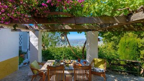 An outdoor dining area with a view of the sea, a pergola, and a table set with plates and glasses.