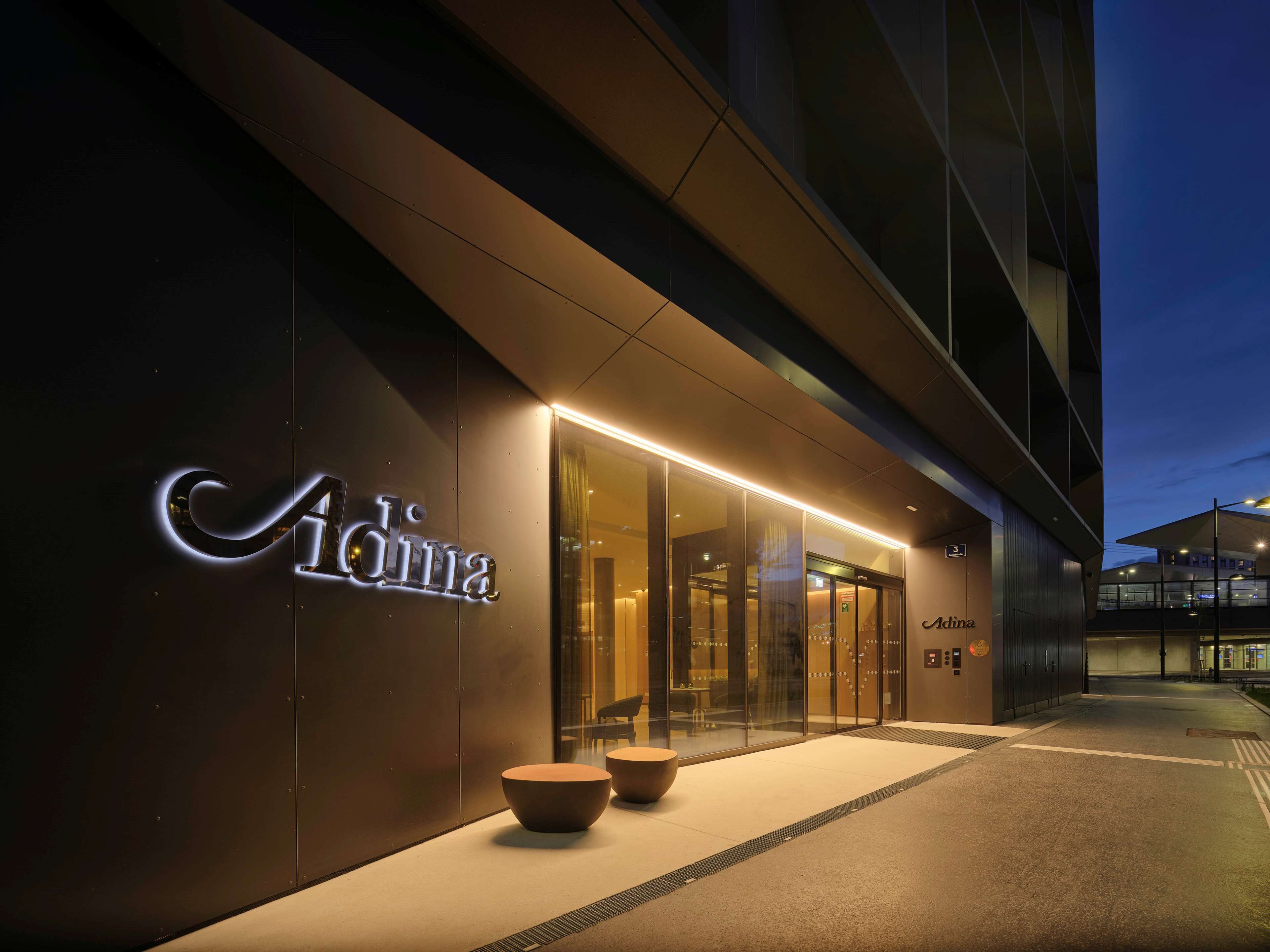 A modern building with a glass entrance and a sign that reads "Adina."