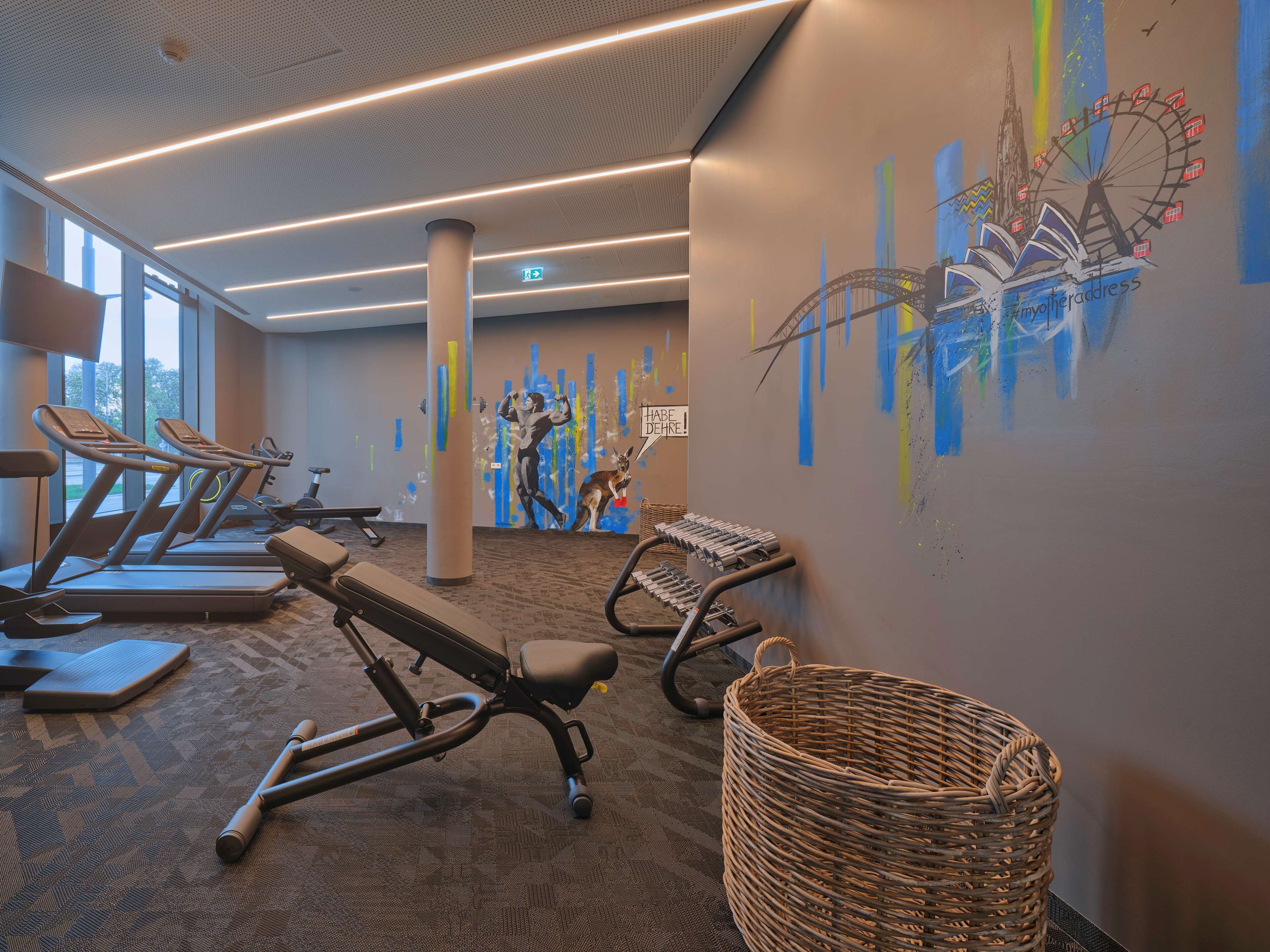 A gym with exercise equipment, a large wall mural, and a large window.