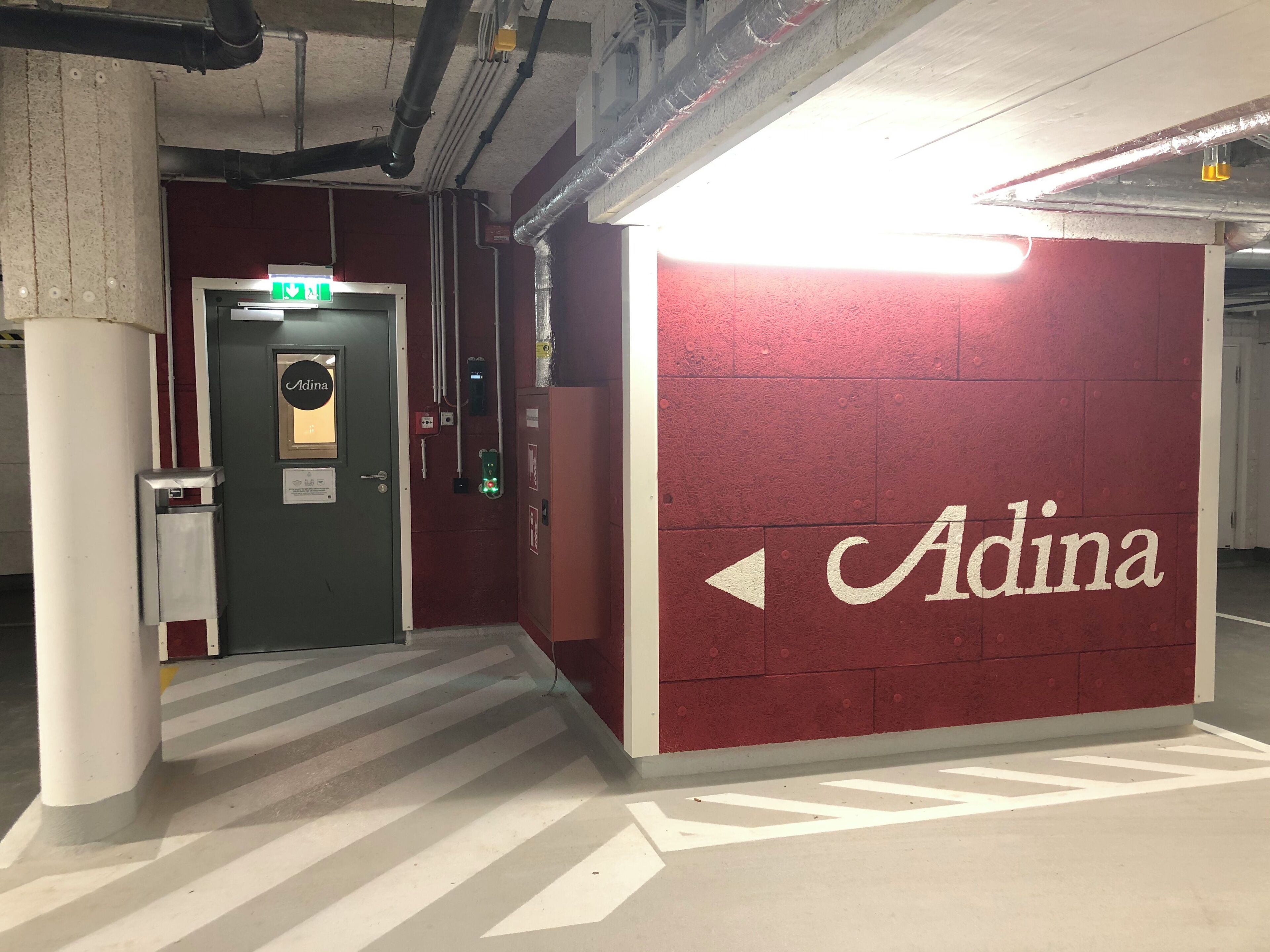 A hallway with a red wall featuring the name 'Adina' and directional arrows.