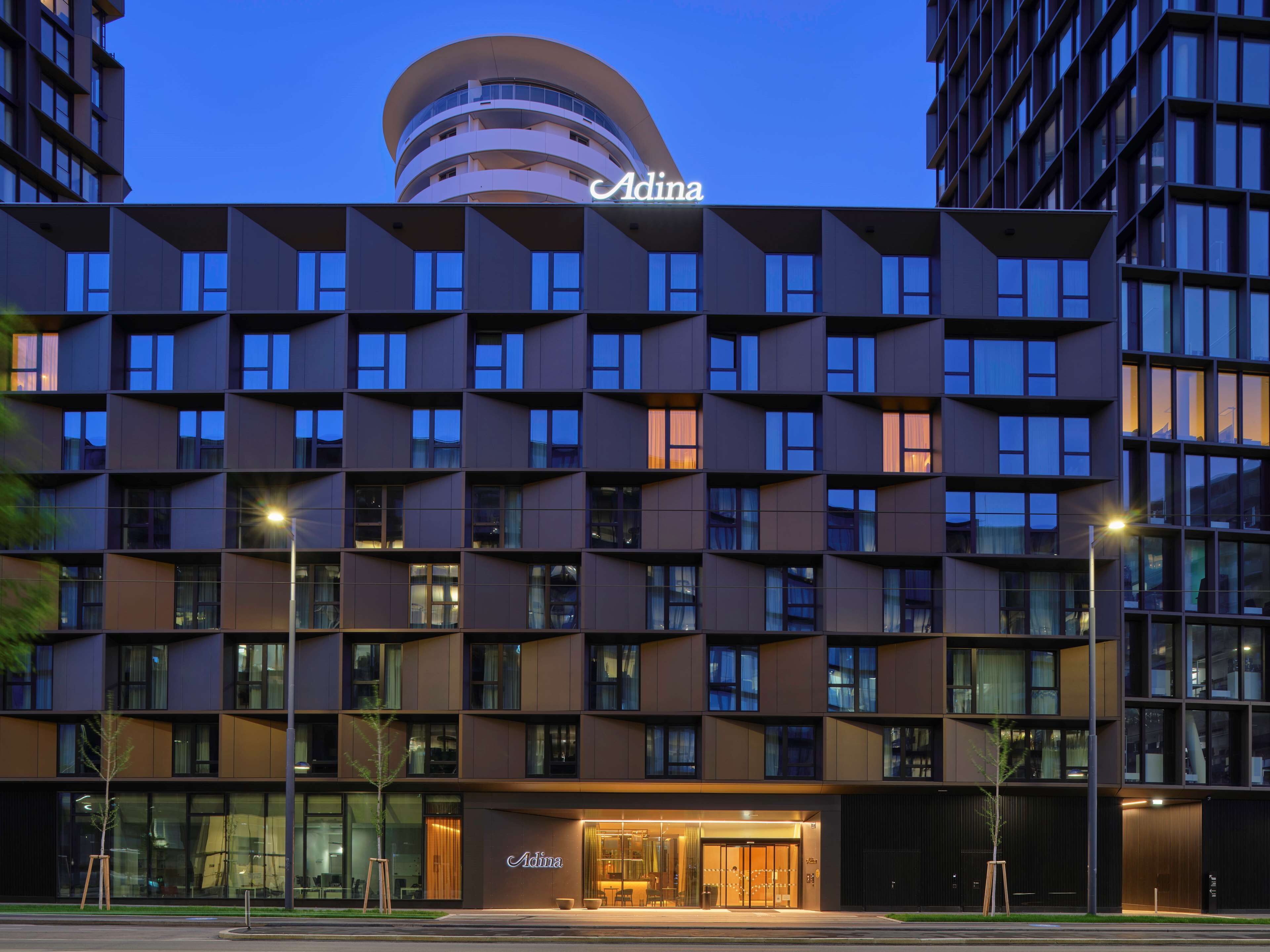 A modern hotel with a distinctive geometric facade, multiple balconies, and a prominent entrance with a glass door.