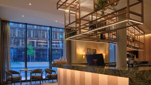 Un moderno vestíbulo de hotel con mostrador de recepción, zona de estar y amplios ventanales que ofrecen vistas del paisaje urbano.