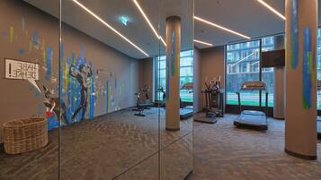 Ein modernes Fitnessstudio mit Trainingsgeräten, großen Fenstern und einem Wandgemälde.
