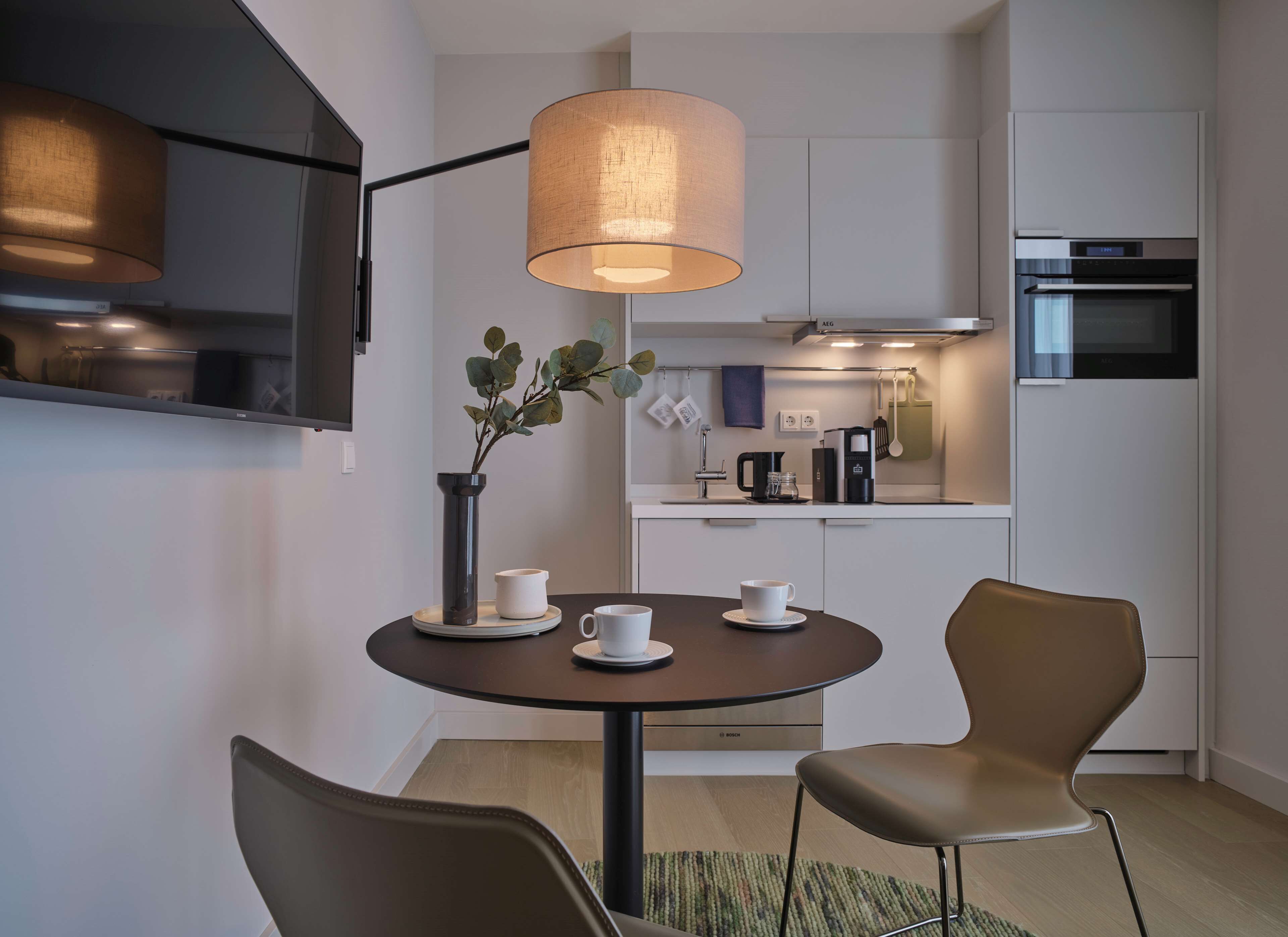 A modern kitchen with a round dining table, two chairs, a hanging light fixture, and a coffee maker.