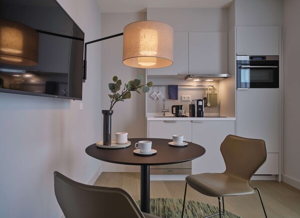 Una cocina moderna con una mesa redonda de comedor, dos sillas, una lámpara colgante y una cafetera.