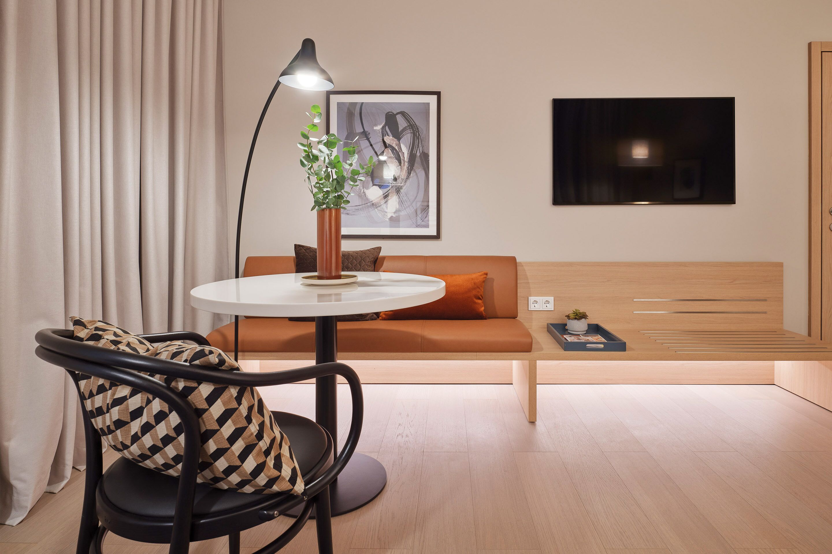 Uma sala de estar moderna com uma mesa redonda, um sofá, uma poltrona, um abajur e uma televisão de tela plana.