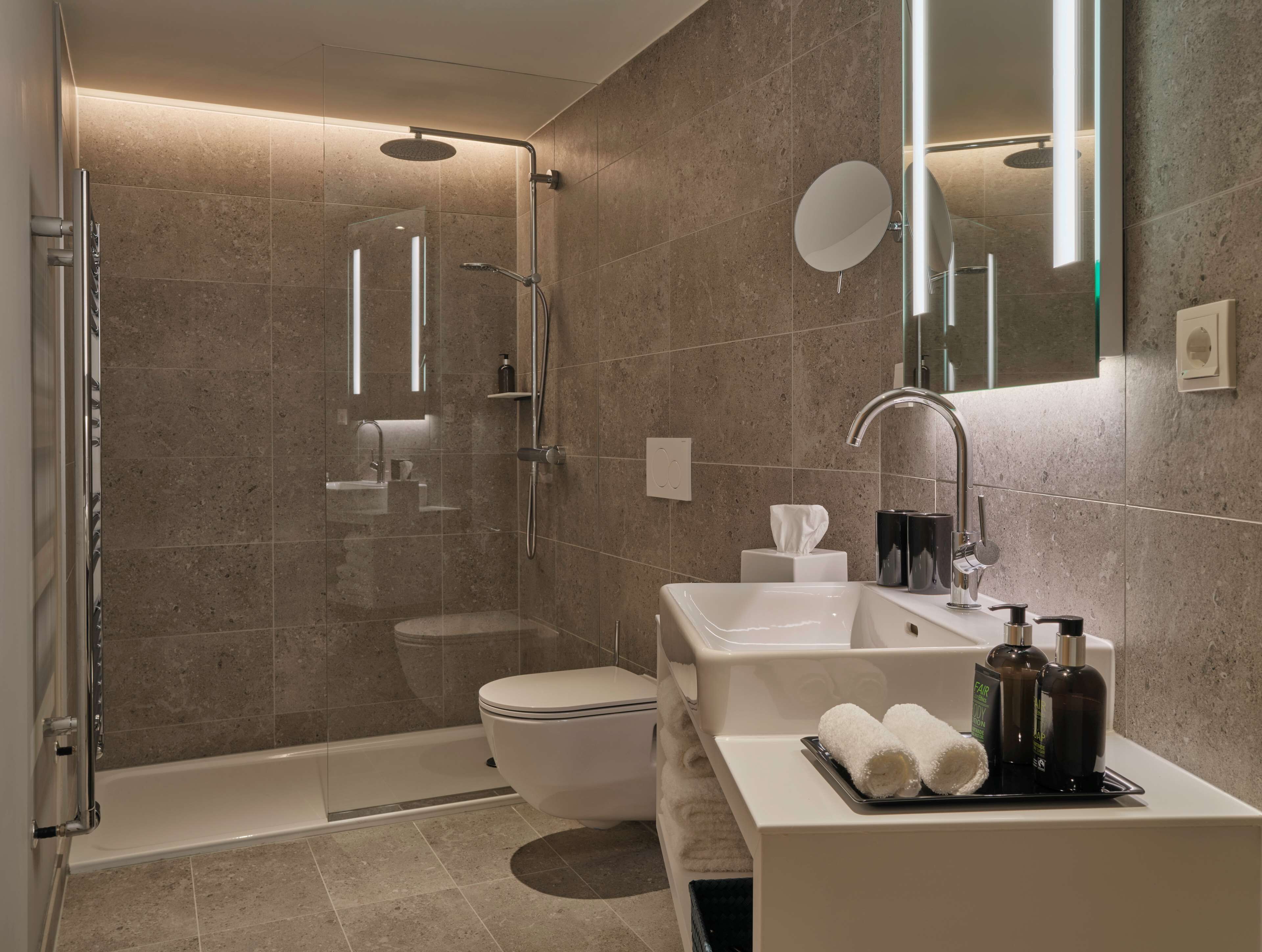 A modern bathroom with a glass-enclosed shower, a white toilet, a sink with a mirror, and toiletries on the counter.