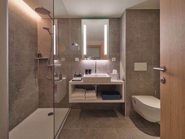A modern bathroom with a glass-enclosed shower, a white sink with a mirror above, and a toilet.