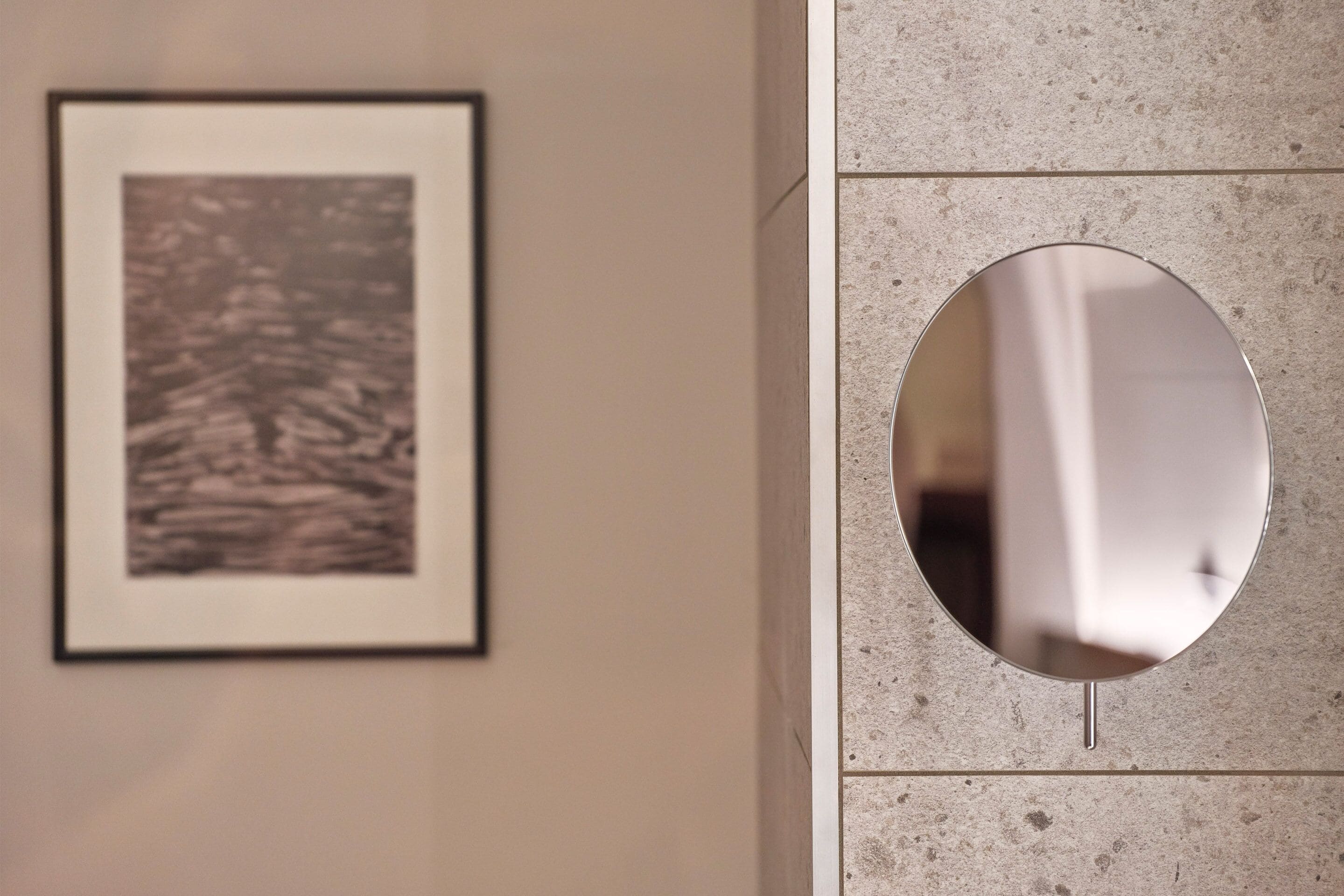 A framed picture on the wall and a round mirror with a metal stand.