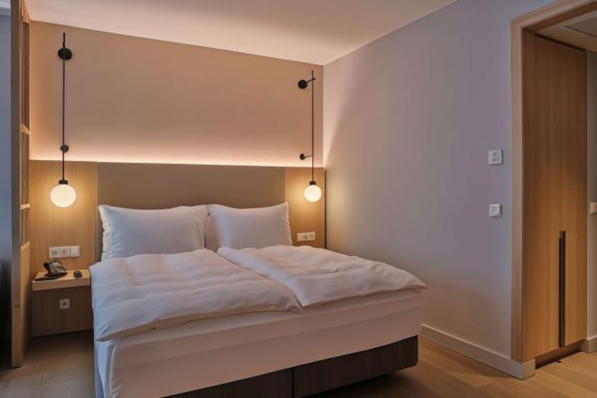 Una habitación de hotel moderna con una cama grande, mesitas de noche e iluminación colgante.