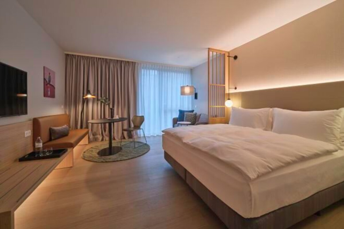Una habitación de hotel con una cama grande, una zona de estar con una mesa y un televisor montado en la pared.