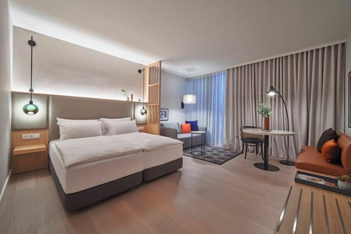 Ein modernes Hotelzimmer mit einem großen Bett, einem Schreibtisch, einem Sofa und einem Essbereich.