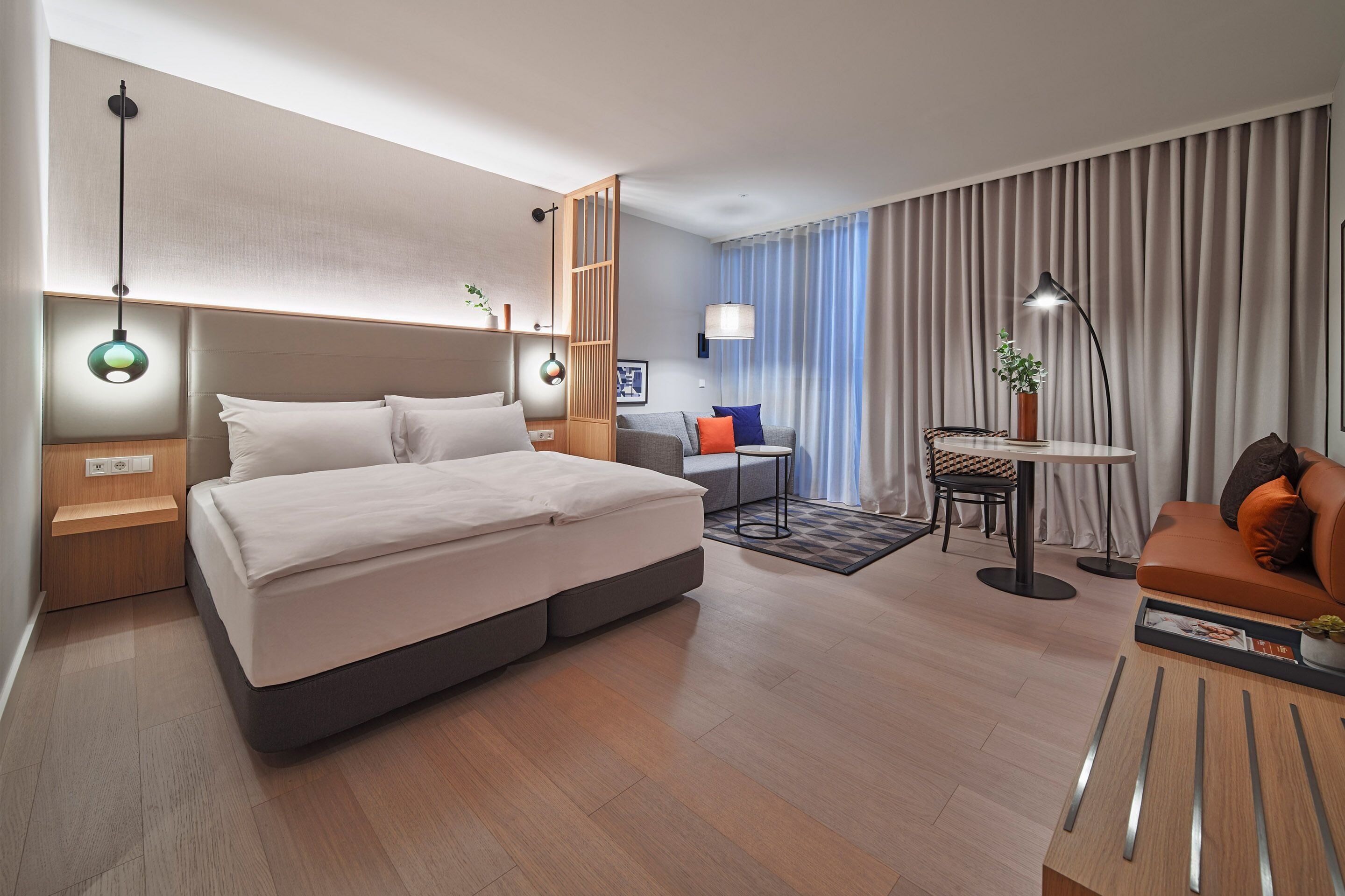 Quarto de hotel moderno com cama grande, mesas de cabeceira, escrivaninha, cadeira e sofá.