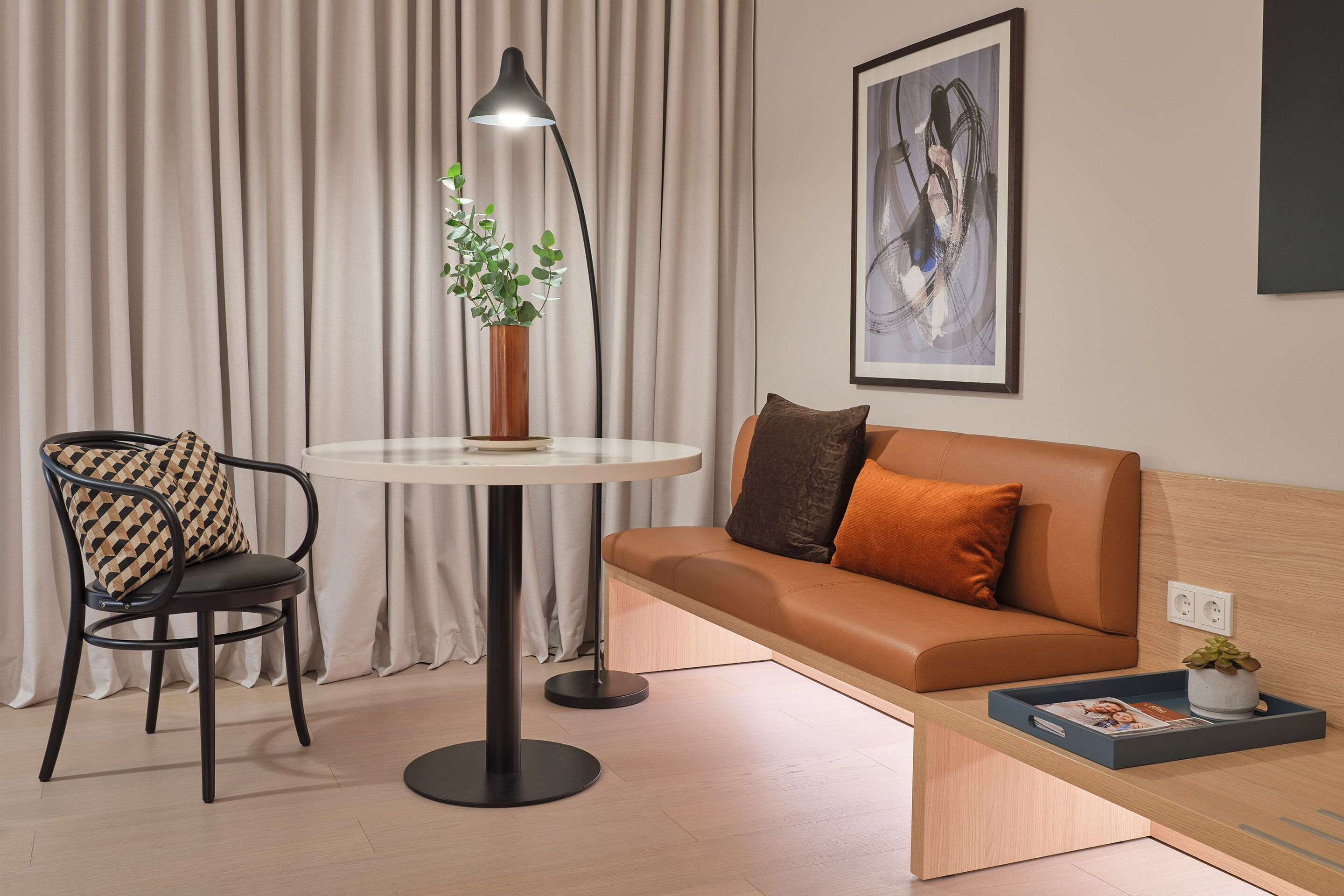 A modern living room with a round table, a chair, a sofa, a floor lamp, and a framed artwork on the wall.
