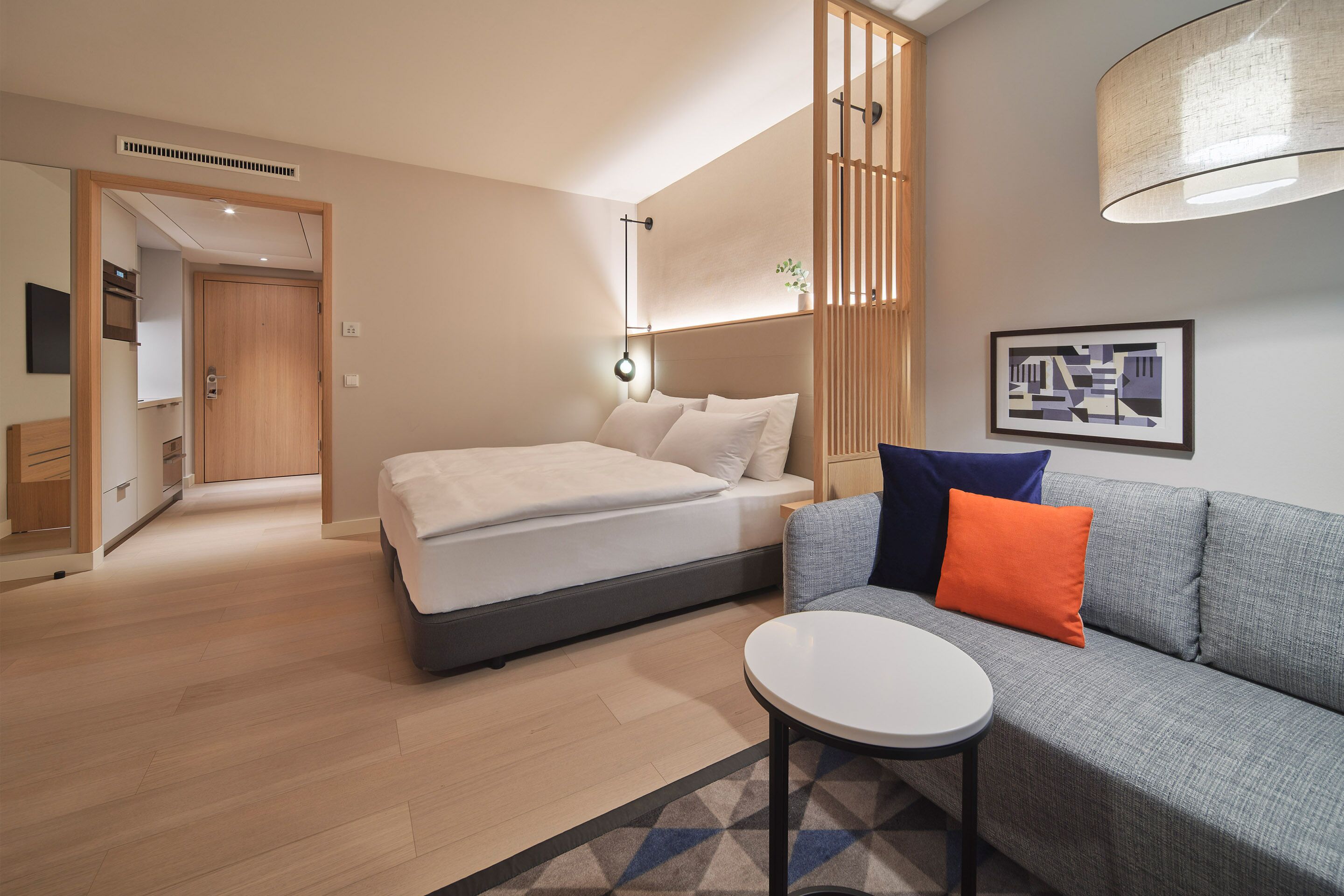 A modern hotel room with a bed, a sofa, a small table, and a wall-mounted lamp.