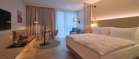 Una habitación de hotel moderna con una cama grande, un sofá, una mesita y un televisor.