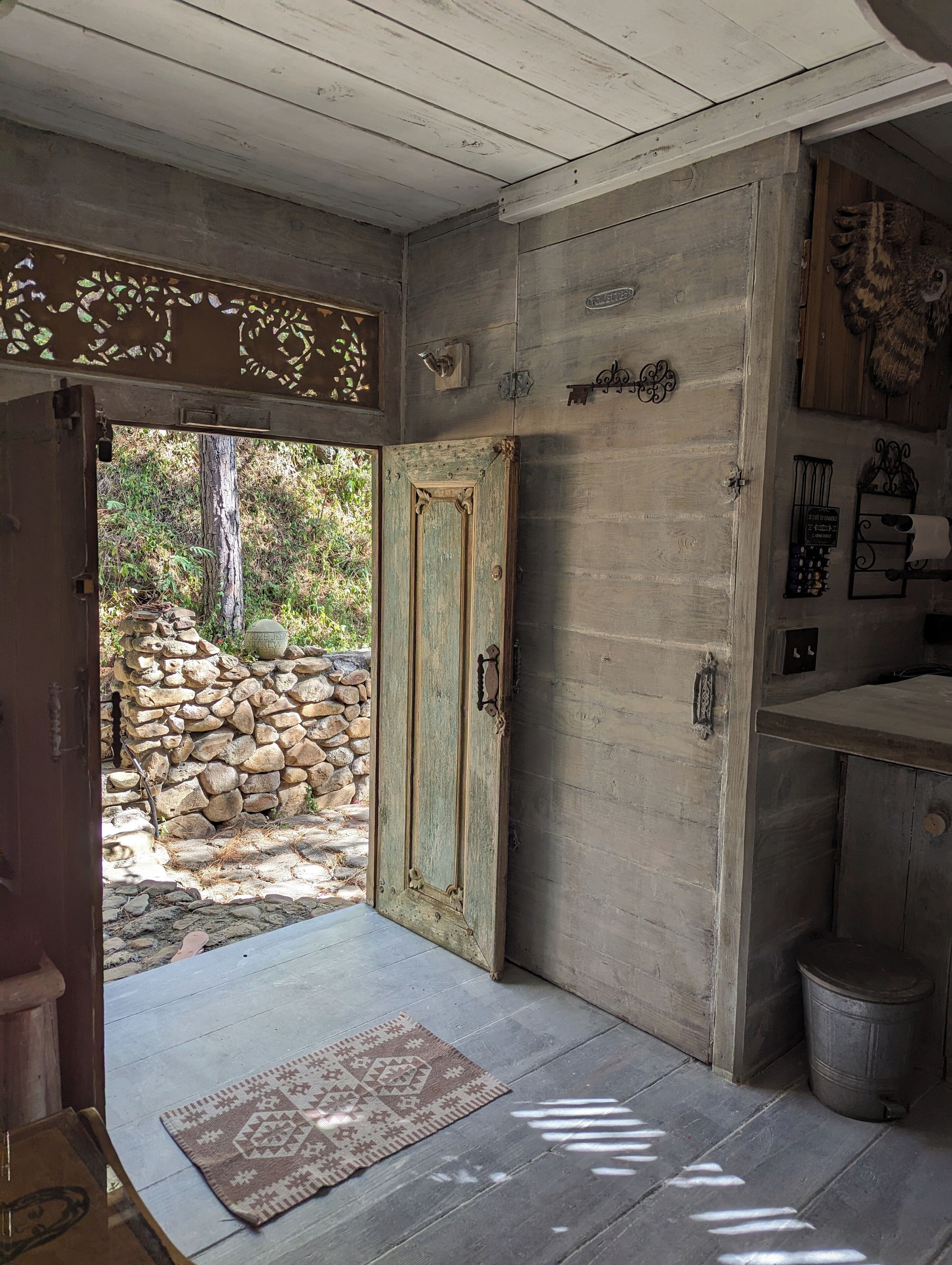 Un interior rústico de madera con una pared de piedra en el exterior, una alfombra estampada y un cubo de metal.