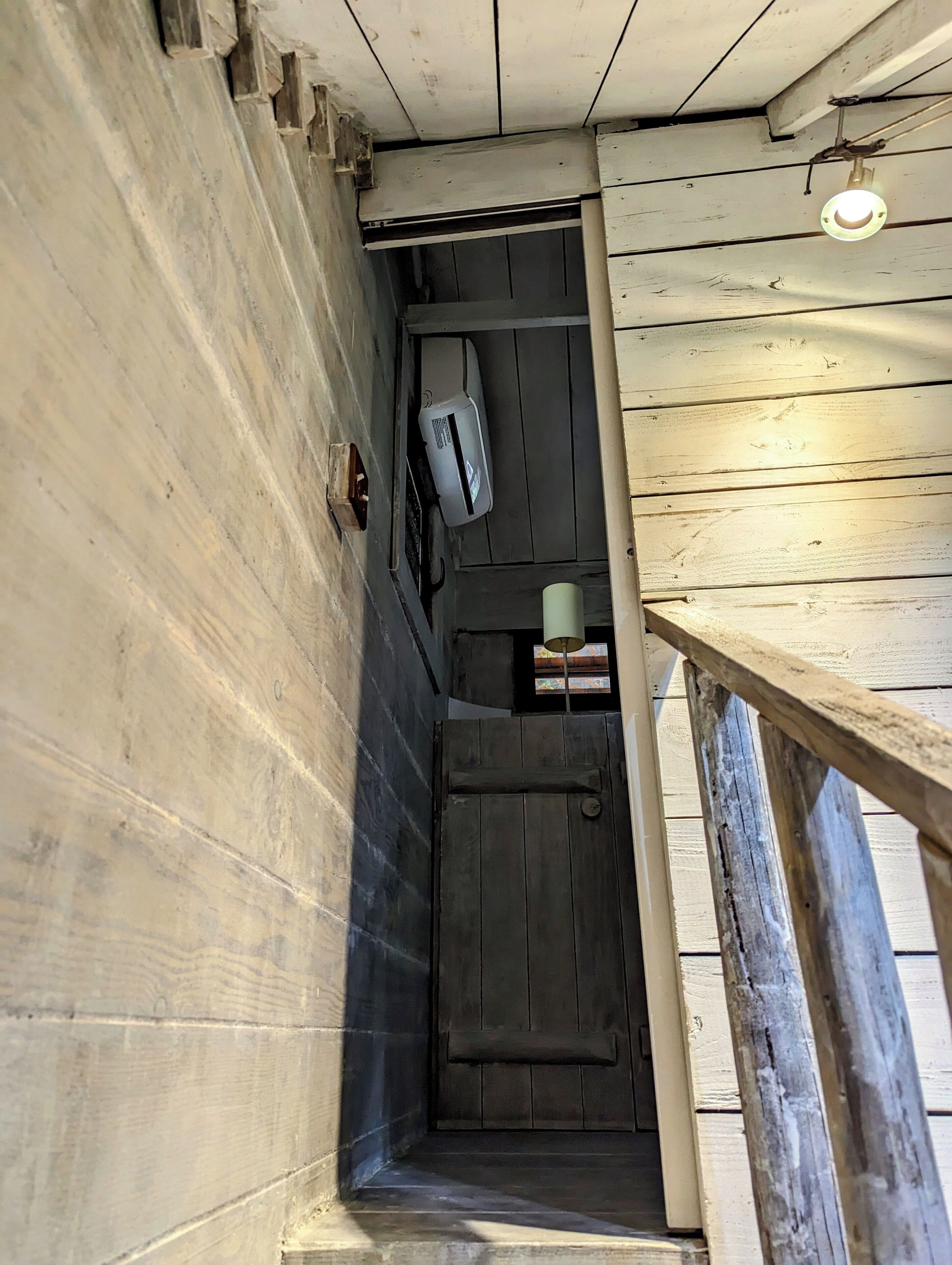 A narrow hallway with a wooden door, a small window, and a light fixture.