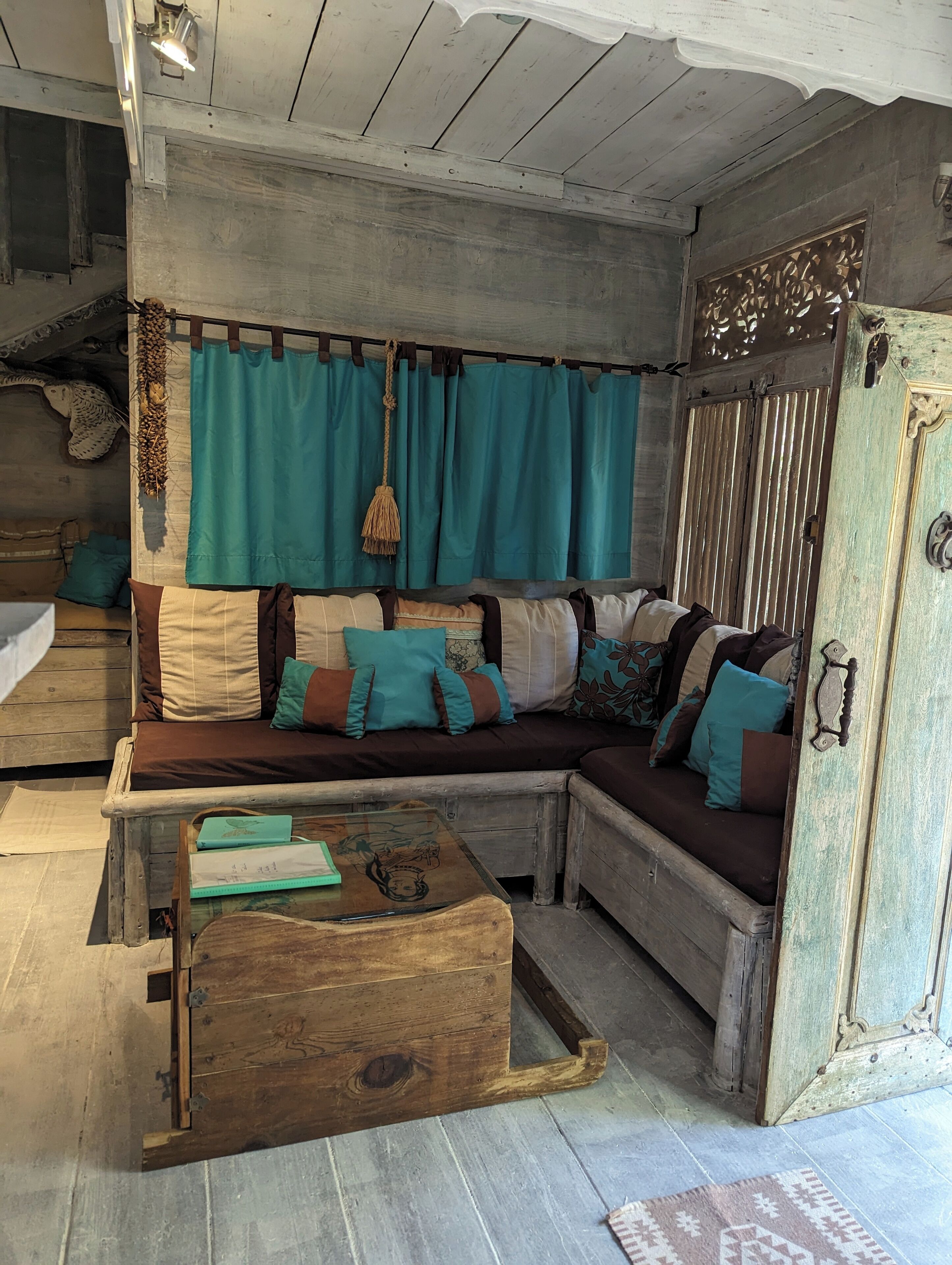 A rustic wooden room with a sofa, teal curtains, and a decorative chest.