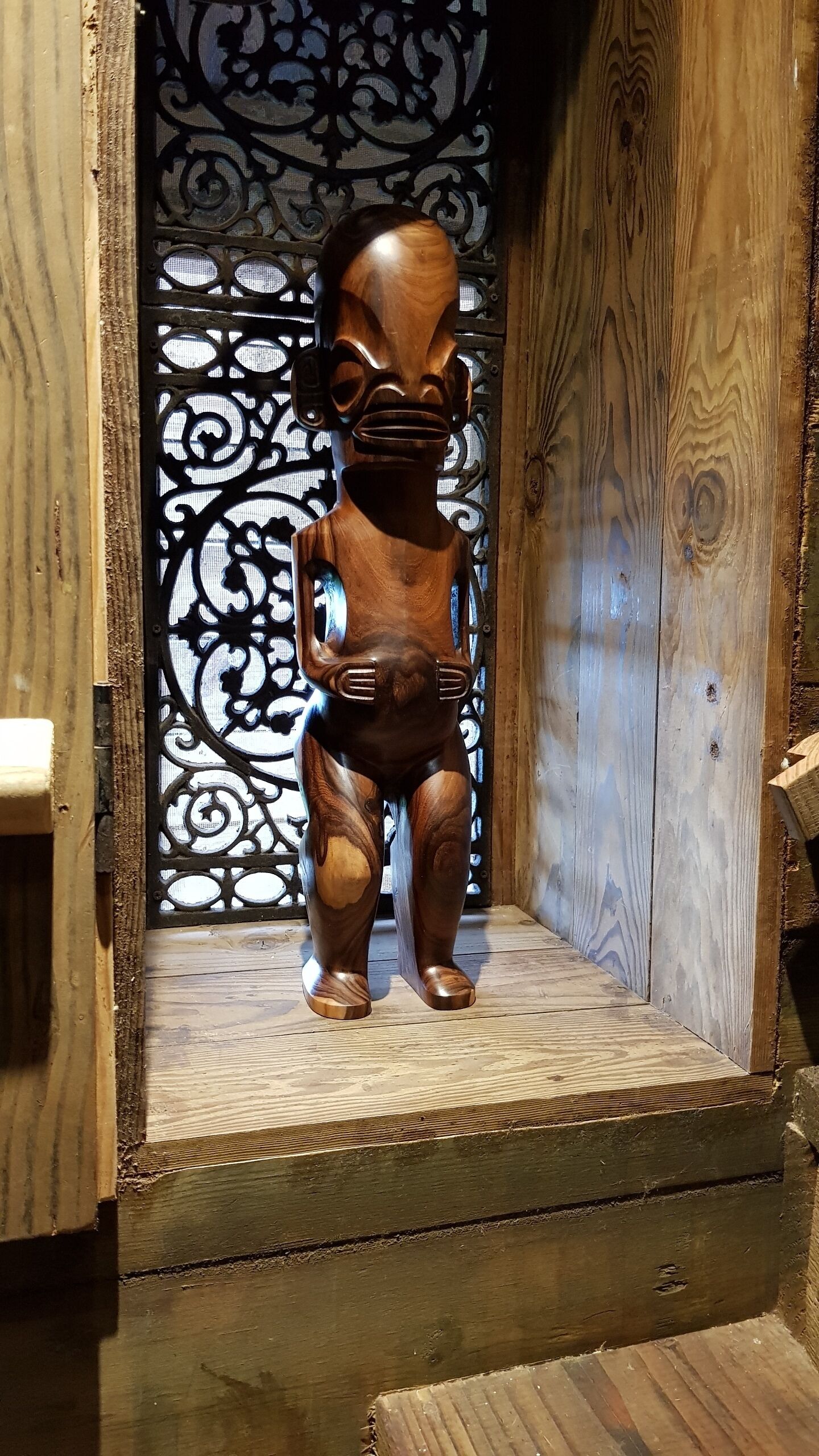 A wooden sculpture of a figure in a niche with a decorative metal screen in the background.